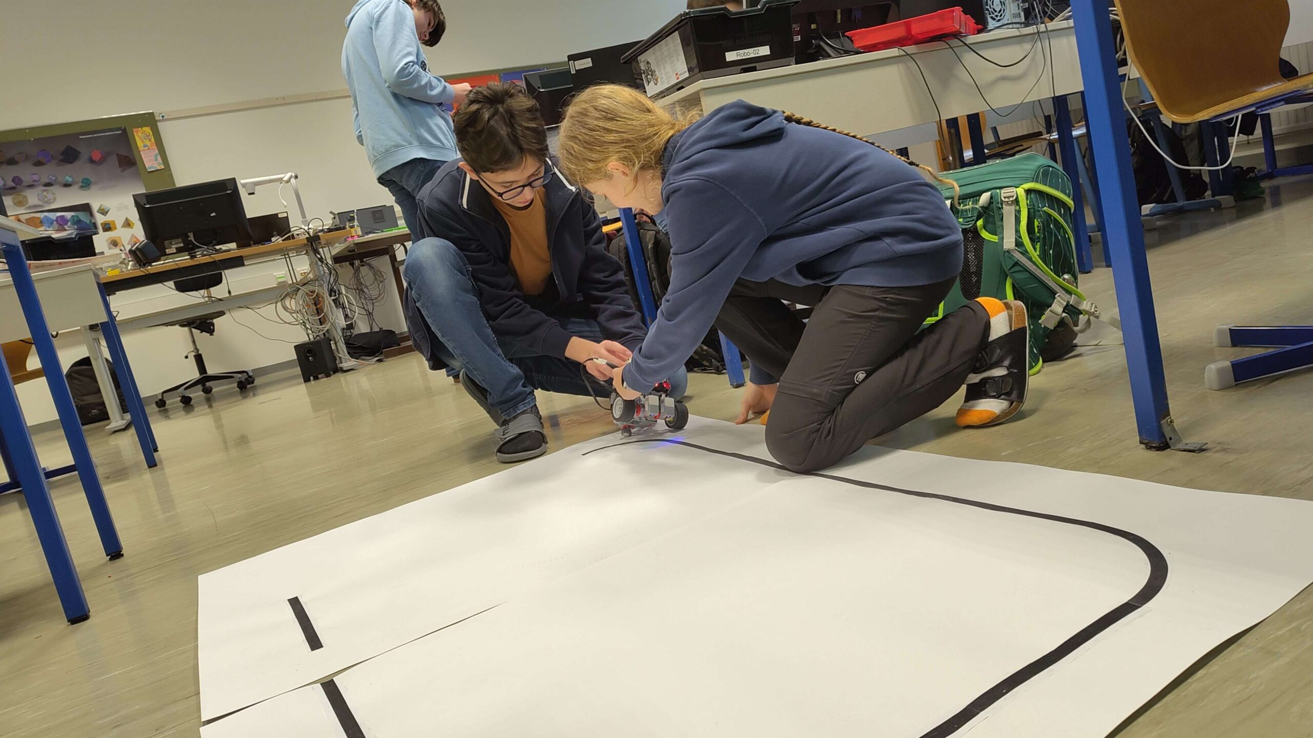 Schüler:innen testen gemeinsam einen Roboter auf einer Fahrstrecke.